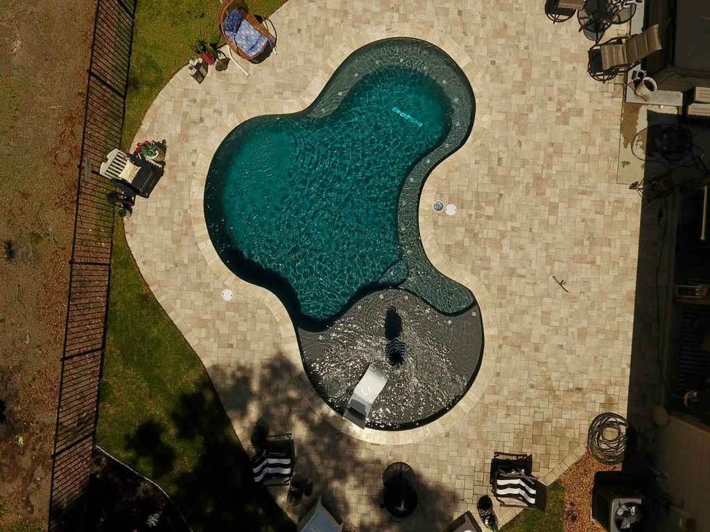 Top 2026 Ocala Pool Remodeling Trends for Your Ocala Home 1 High Angle Drone View Of A Kidney-Shaped Backyard Swimming Pool With Dark Plaster, A Wide Tanning Ledge, And Tan Paver Decking Surrounded By A Black Fence