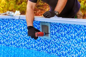 A Close-Up Of A Pool Technician'S Hands In Black Gloves Using A Power Drill To Secure A Skimmer Faceplate Onto A Blue Mosaic-Patterned Vinyl Pool Liner. Led Pool Light Installation And Repair In Ocala.