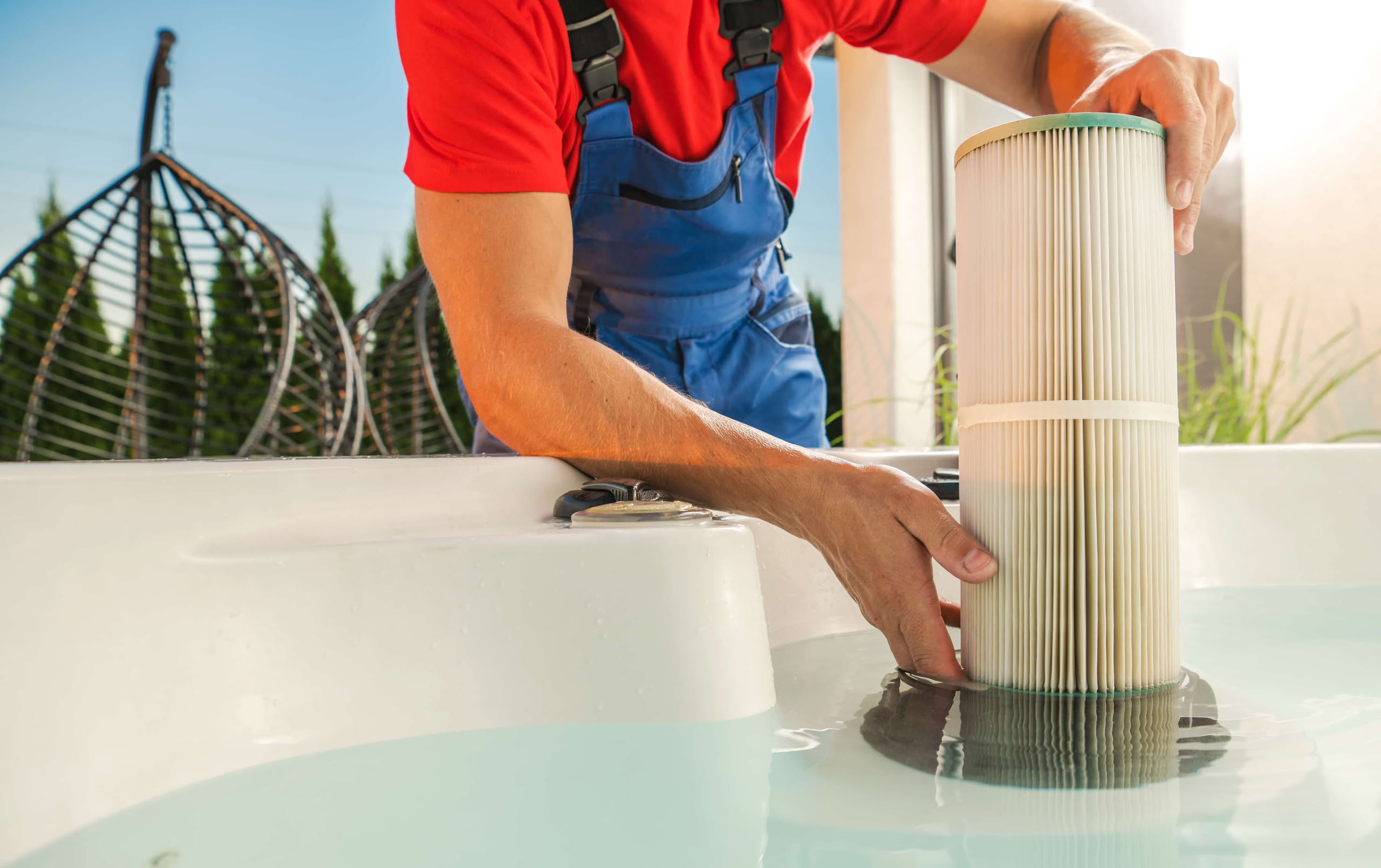 Professional Pool Filter Cleaning Services in The Villages: Ultimate Guide 1 Close-Up Of A Service Technician In Blue Overalls Inserting A New White Pleated Cartridge Filter Into The Filter Housing Of A Hot Tub Filled With Clear Water.