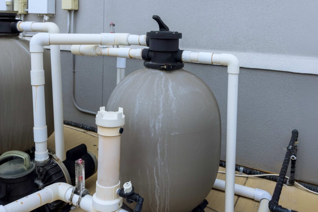 A professional-grade sand filter tank and PVC piping system for a residential outdoor swimming pool filtration system.