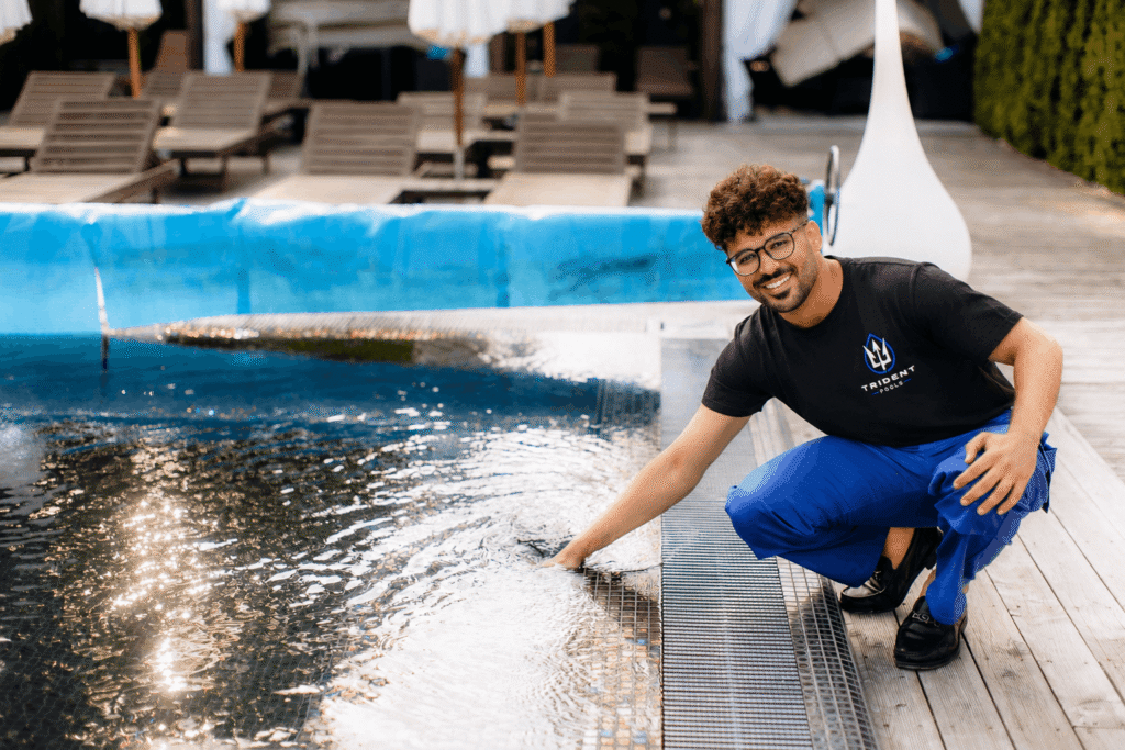 A professional pool technician from Trident Pools wearing a company shirt checks the water quality of a swimming pool in Miami, FL.